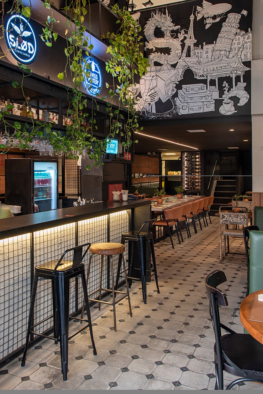 Bar do Belô em Belo Horizonte: bancos altos no balcão, plantas pendentes, letreiro luminoso e mural ilustrado sobre piso hidráulico.