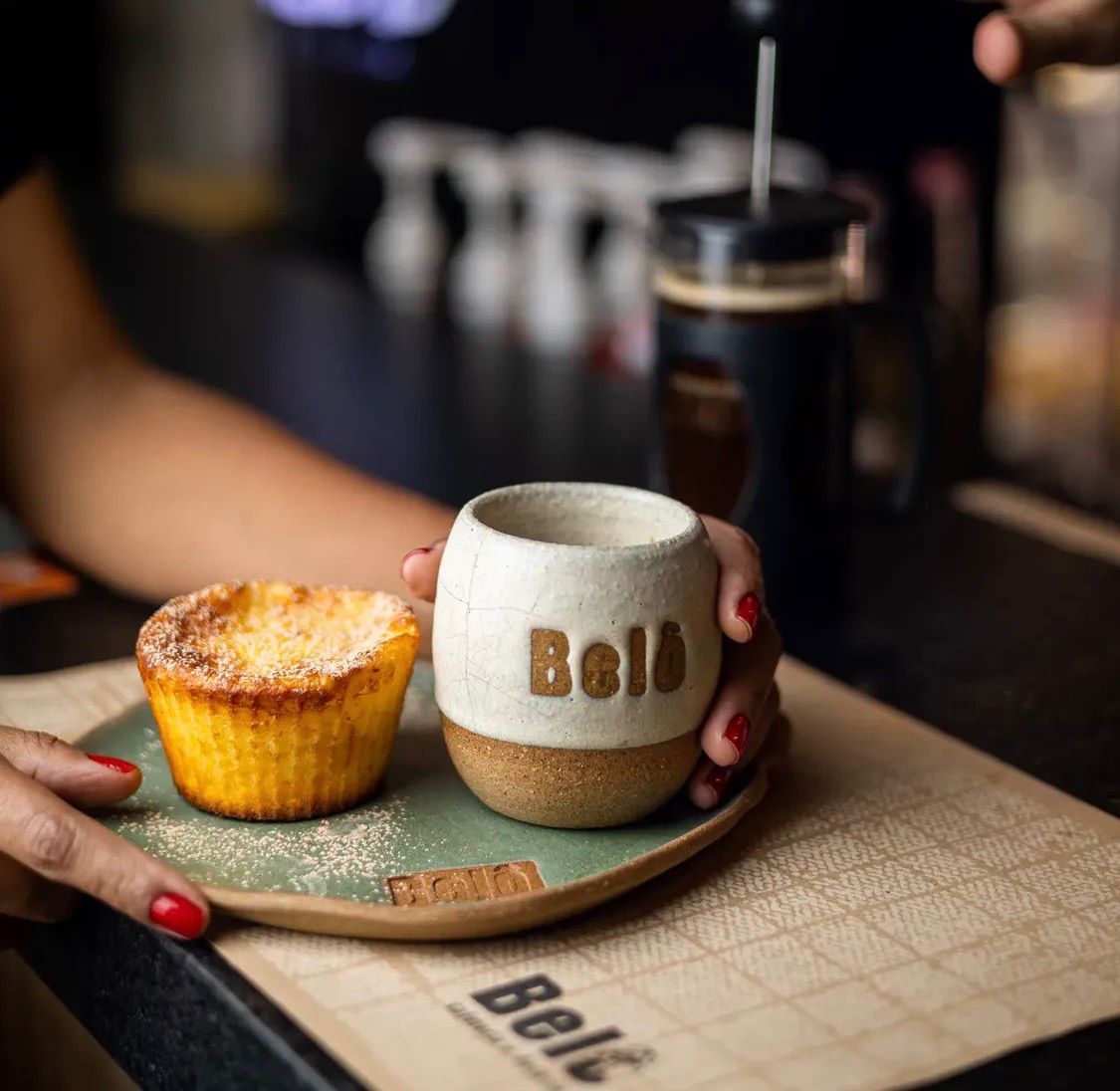 Café servido em xícara de cerâmica artesanal ao lado de um bolinho individual.