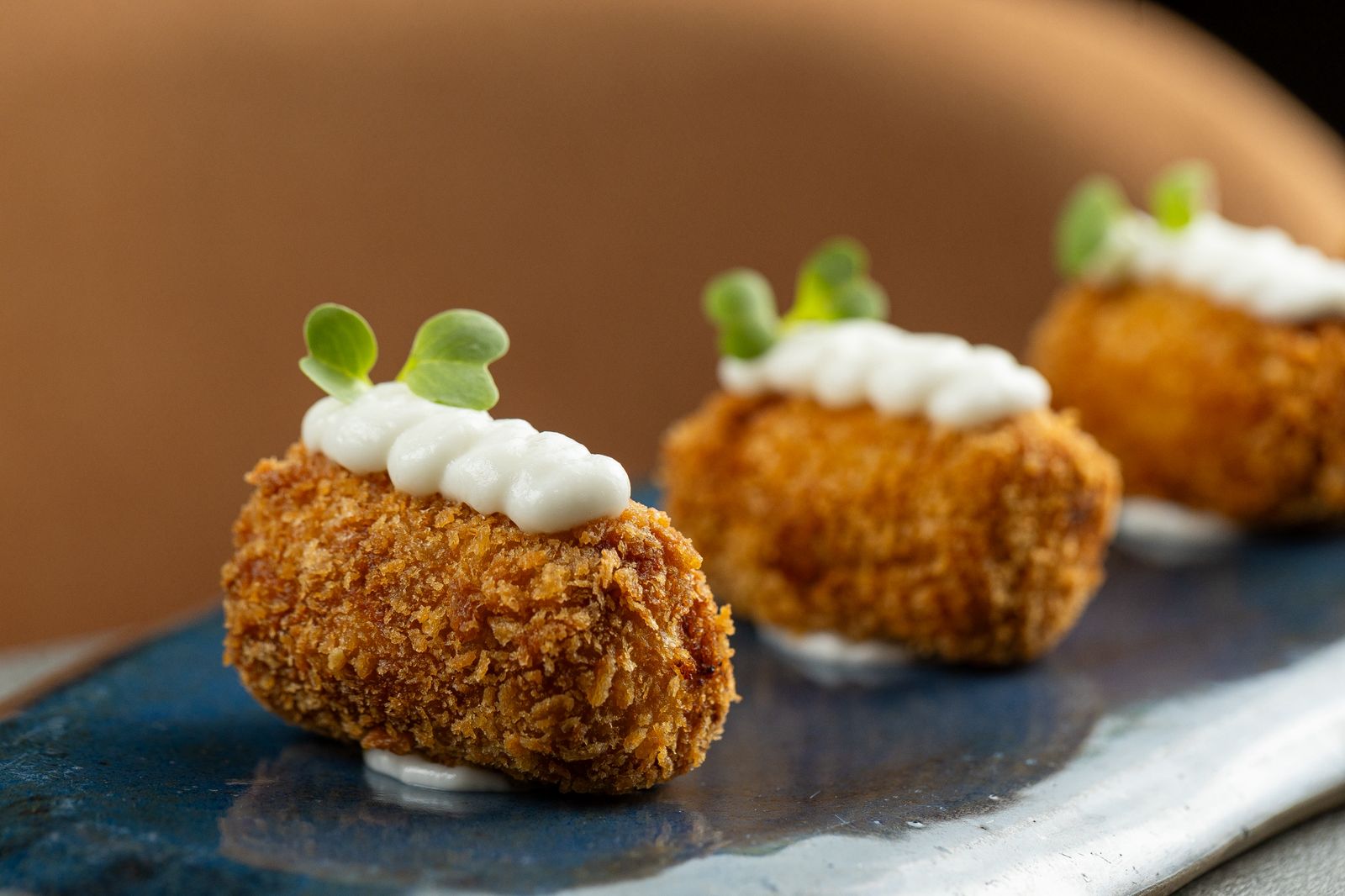 Croquetes dourados com creme branco e ervas finas em prato escuro.