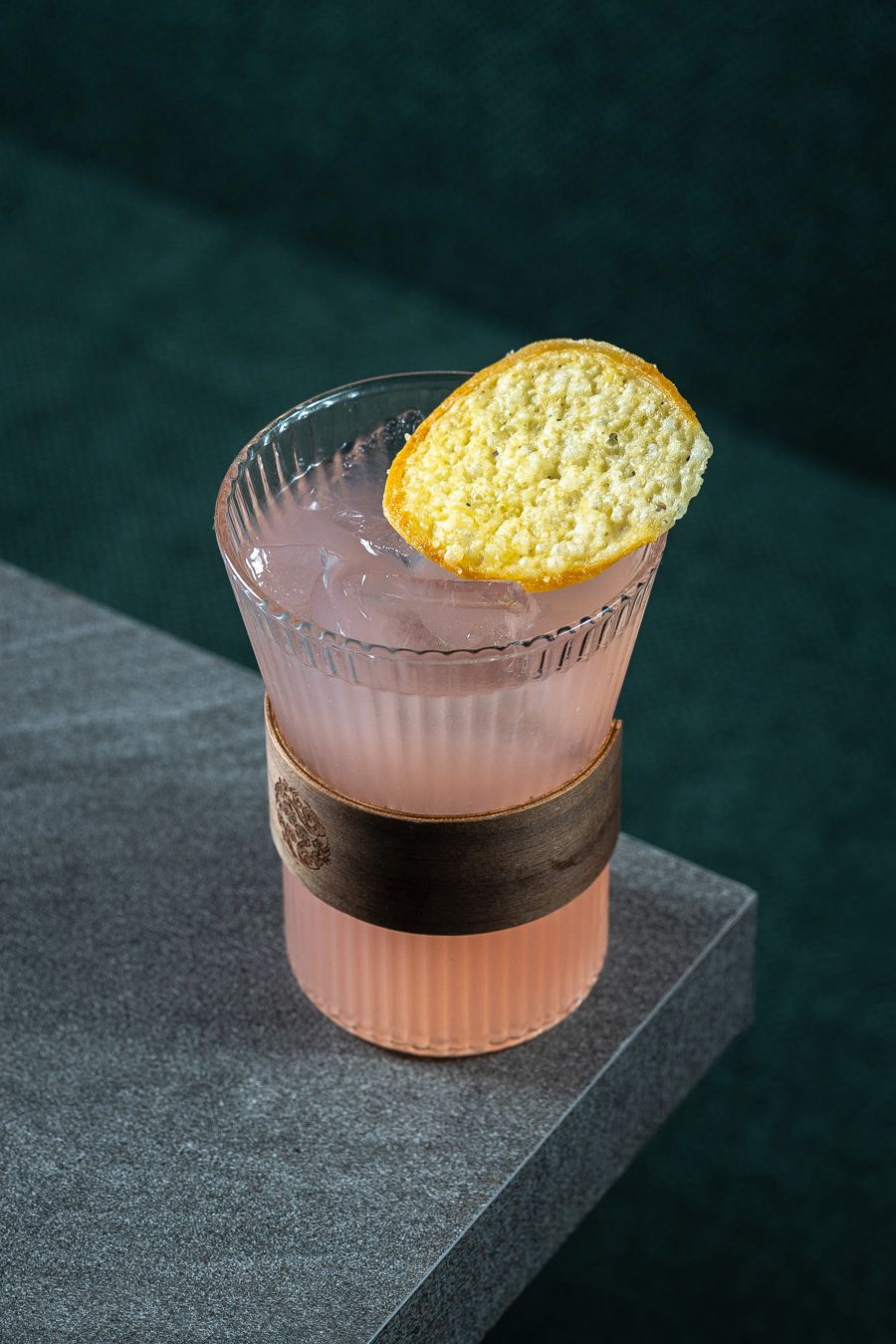Drink rosado com guarnição cítrica sobre balcão escuro.
