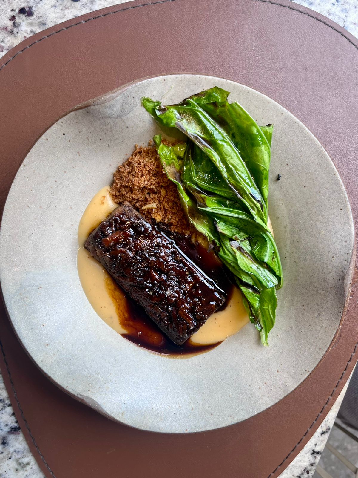 Carne laqueada com folhas verdes e creme em louça clara, fotografada em close.